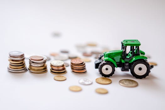 A miniature green tractor beside stacks of coins in a creative still life scene.